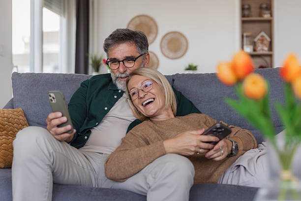 istock Mature couple relaxing on sofa sharing smart phone 2240810943