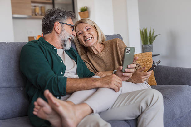 istock Senior couple relaxing on couch sharing smartphone laughing 2240811511