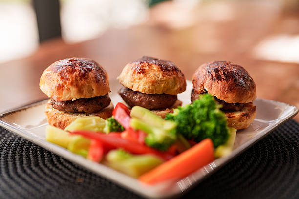 Three tender mini beef burgers served with a colorful side of steamed broccoli, carrots, and bell peppers. A lighter, balanced take on the burger experience, combining rich flavor with fresh, healthy sides.