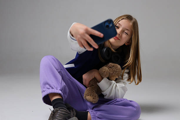 istock Caucasian young girl taking selfie with phone and teddy bear in studio setting 2240812346