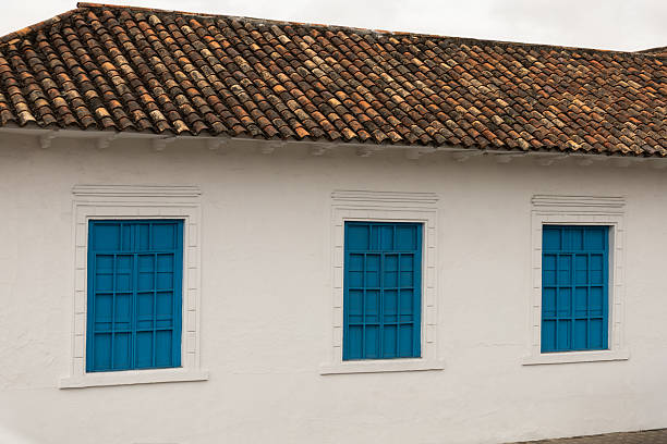 istock Traditional colonial white facade featuring three bright blue wooden windows under a rustic tiled rooftop in a quiet street 2240815044
