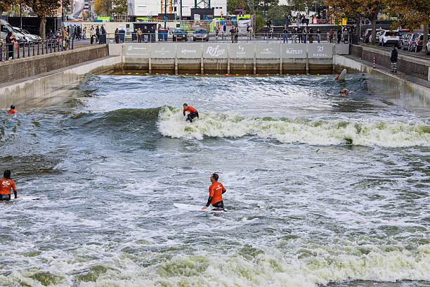 A close-up of surfers wearing orange vests riding and waiting for waves in the artificial urban surf spot, RiF010, located in a Rotterdam canal. Rotterdam, Netherlands. 19 October 2025.