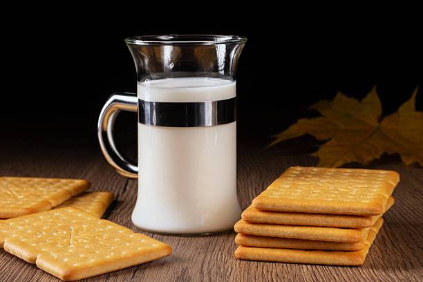 This charming photo highlights a glass of creamy milk accompanied by a plate of salty crackers on a vintage kitchen table, symbolizing comfort and simplicity in meal times.