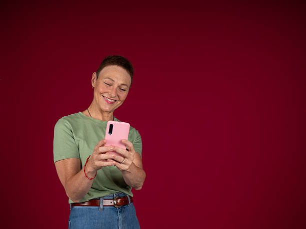 istock Mature woman smiling using mobile phone against red background 2240825514