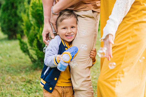 Smiling little boy holding bubble gun outdoors, playing with parents and enjoying joyful family time in the garden.