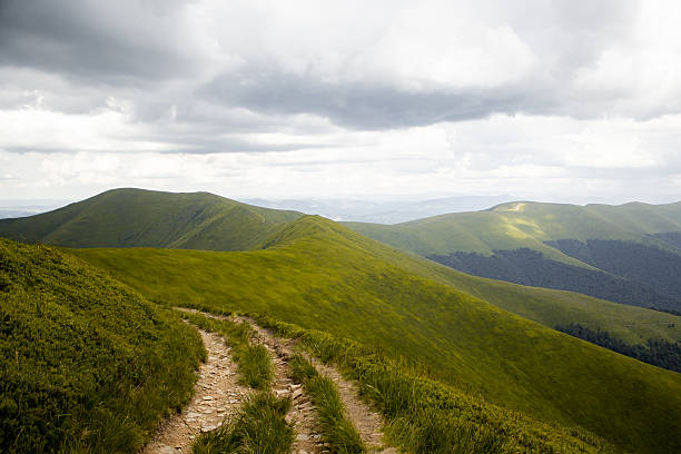A scenic mountain trail winding through green hills under dramatic clouds — a path that inspires adventure, reflection, and the journey toward new horizons.