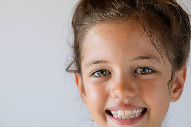 A cheerful young girl with a messy bun smiling brightly against a plain white background. The image captures joy, innocence, and childhood happiness in a natural and positive way.