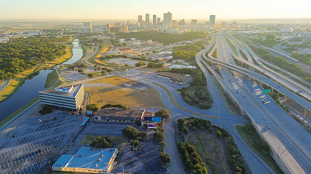 istock Stacked interchange near Fort Worth divides downtown skyline from industrial logistics zone, elevated ramps, freight access, and golden hour light casting long shadows across both sectors, Texas 2240836304