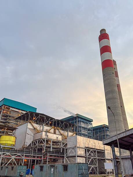 istock Industrial complex featuring towering red and white striped smokestacks against a cloudy sky at dusk 2240841619