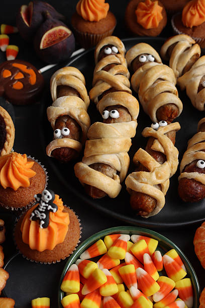 Stock photo shows a spooky Halloween candy corn sausage mummies make a fun and festive party food display. Wrapped in pastry with candy corn details, these creative snacks are both cute and scary