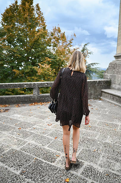 Woman with blonde hair and tattoos walking away on a stone path during autumn