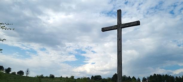 istock Wooden Cross Standing in a Green Field Under Dramatic Clouds 2240844106