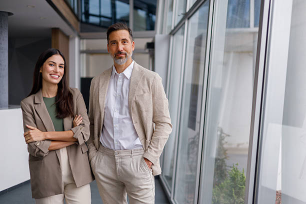 istock Business colleagues standing in modern office building corridor, smiling, collaborating, and looking at camera 2240844245
