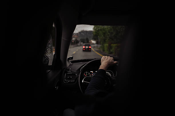 Adult person driving a car in rainy weather, holding the steering wheel