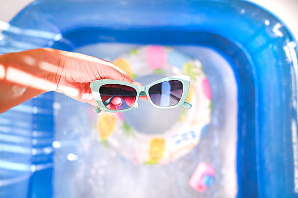 Hand holding sunglasses over water in a blue inflatable pool