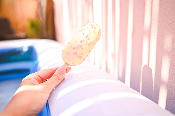 Person enjoying sweet frozen dessert on a sunny summer day by inflatable pool
