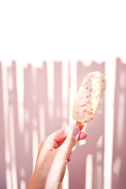 Hand holding a refreshing ice cream popsicle covered in white chocolate and pink sprinkles