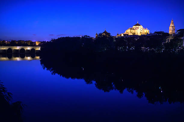 Twilight casts golden hues on the Guadalquivir, with the Roman bridge to the left and the Mosque-Cathedral illuminating the scenery.