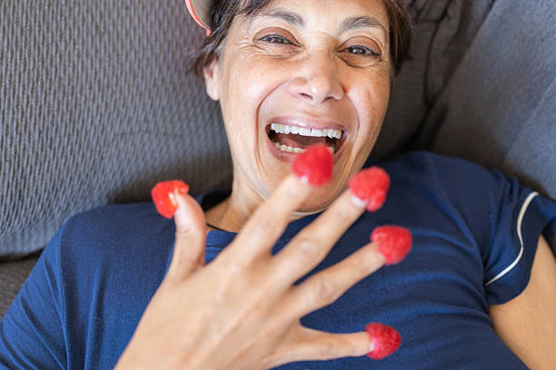 Mature woman laughing with raspberries on her fingertips