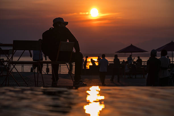 Seattle, USA - Aug 26, 2025: A sitting person watches the hazy climate fire sunset at the new Pier 58.