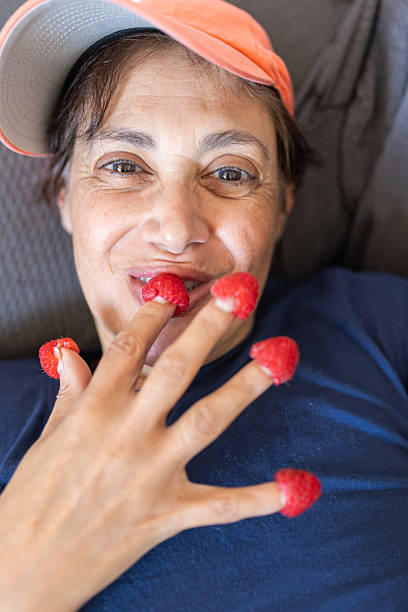 Smiling middle eastern woman enjoying ripe red raspberries, placing them on her fingertips like playful finger foods and on her lip, highlighting healthy eating with a fun attitude