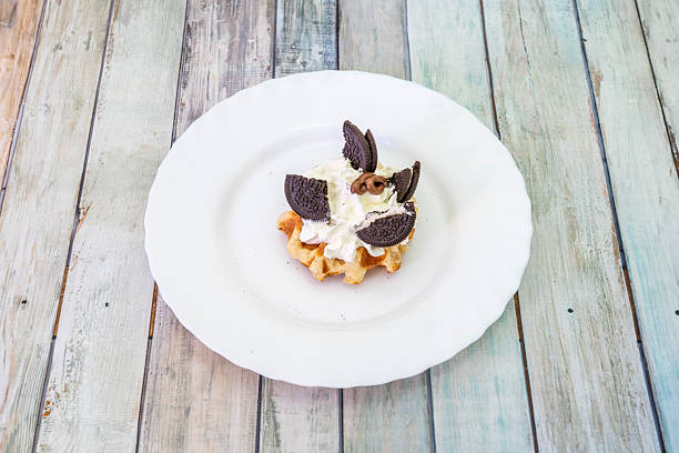 Crispy waffle-shaped cake of Belgian origin that is cooked between two plates, to this was added a lot of cream, cookies with chocolate chips on a white plate