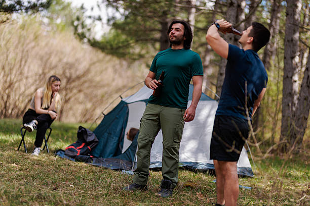 istock Friends enjoying camping outdoors with drinks in nature, surrounded by trees and a tent on a sunny day 2240865252