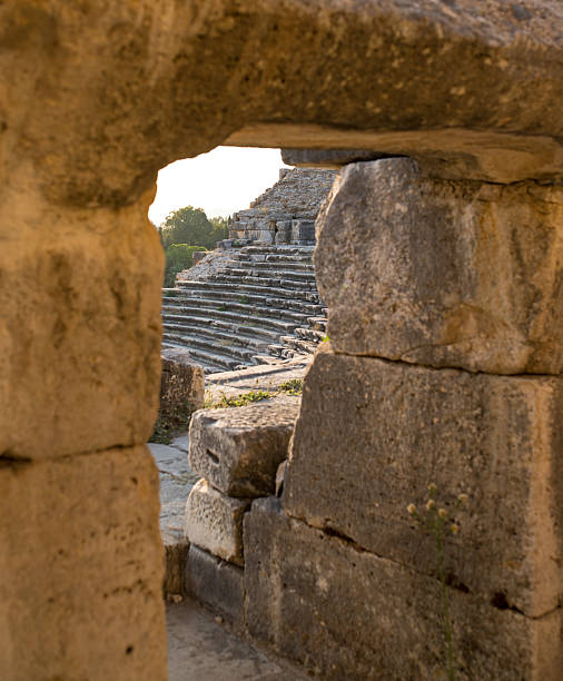 A captivating view of an ancient amphitheater through a stone-framed opening, showcasing worn steps and a scenic sunset. The warm hues add depth and emphasize the historical essence of the relic.
