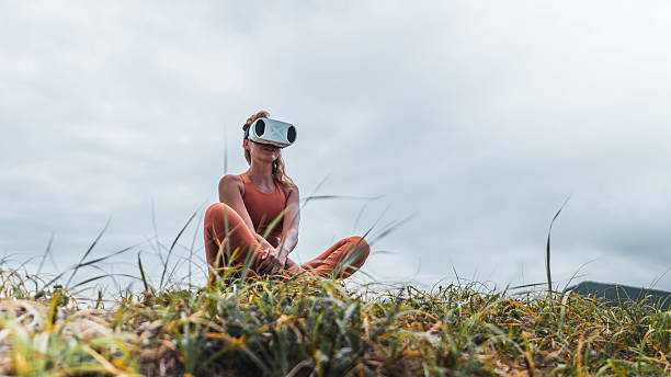 istock Female in sportswear practicing relaxation with VR headset on grass. Combination of modern technology, meditation, and outdoor lifestyle. Perfect for concepts of future health and virtual wellness. 2240885209