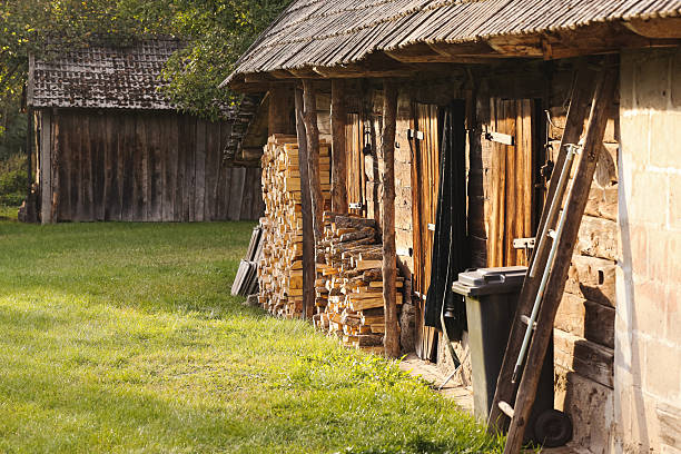 istock Old wooden barn with stacked firewood and tools outside on sunny day. 2240896205