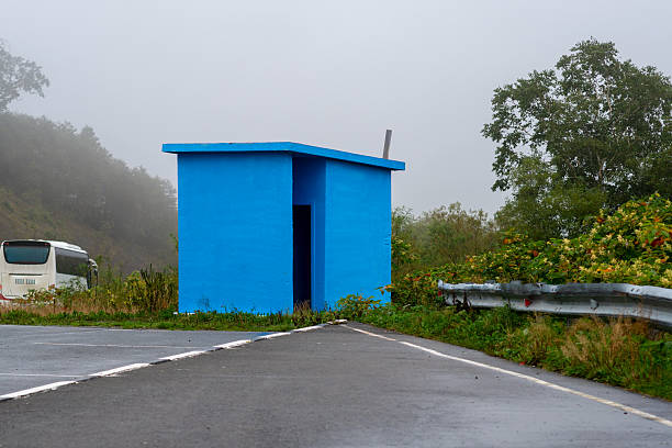 A vivid blue roadside building stands out against foggy surroundings with greenery, asphalt, and a bus partly visible in the misty background.