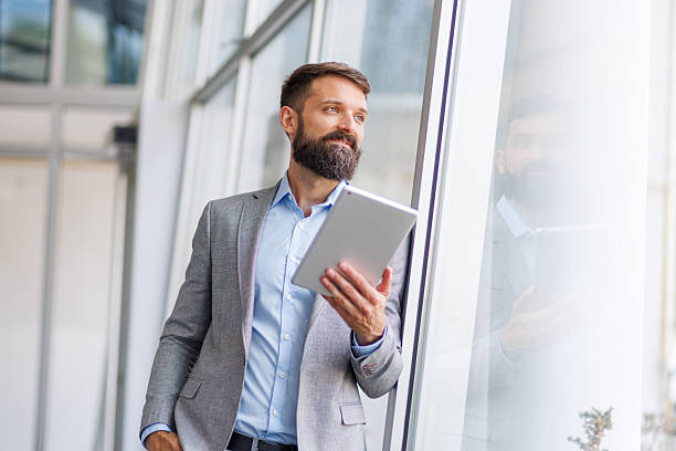 istock Businessman holding tablet looking out office window 2240905964