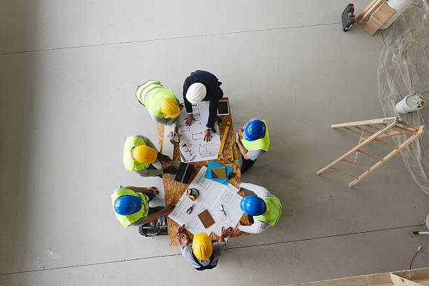 istock Above view of architect and manual workers working on plans at construction site. 2240908621