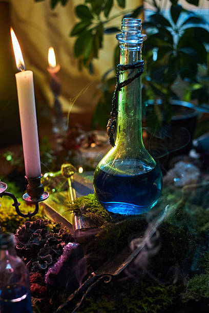 istock blue potion sits in a glass bottle on a moss-covered table. Flickering candles cast a warm glow, while plants add to the enchanting atmosphere of the space 2240910628
