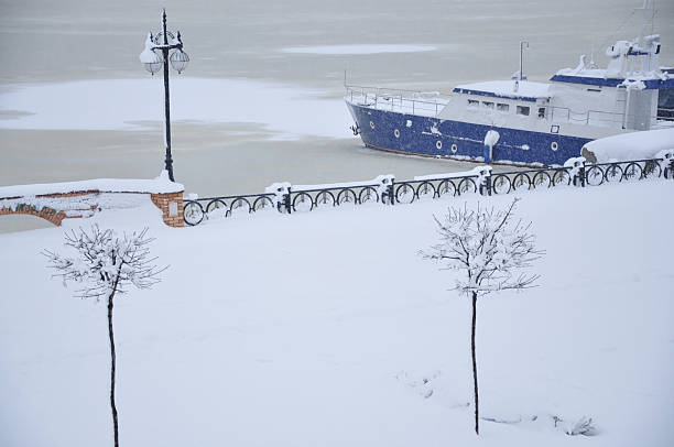 A blue boat rests quietly at a snow-covered pier as winter blankets everything in white. Calm and stillness reign by the frozen waterfront.