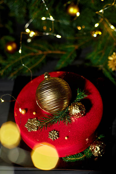 istock A vibrant red cake sits elegantly on a dark surface, decorated with golden orbs and festive greenery, creating a joyful atmosphere with twinkling holiday lights. 2240912390