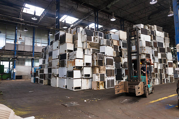 Interior of a large recycling plant with used refrigerators collected for dismantling and metal recovery, worker driving a forklift