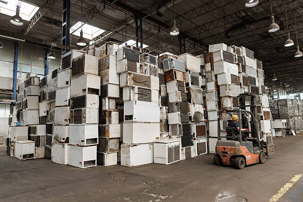 Recycling warehouse where skilled worker operating forklift near piles of electronic scrap and machinery
