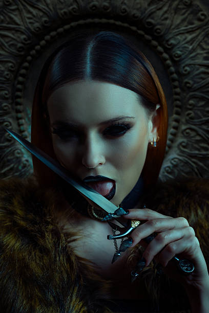 Moody portrait of a gothic woman with black lipstick and sharp nails, provocatively licking a dagger while wearing fur and dark accessories.
