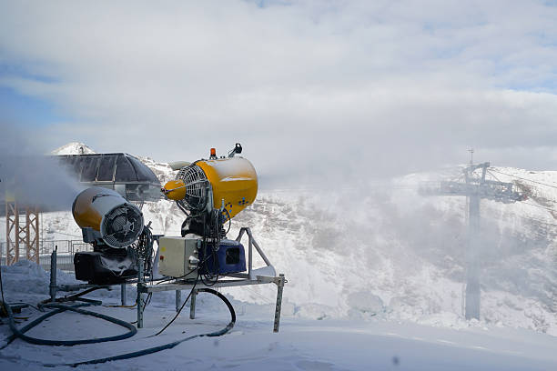 Industrial snow cannons producing artificial snow in a mountainous area for ski resort preparation. Represents winter sports technology, cold climate infrastructure, and outdoor mountain environment.