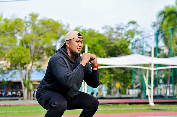 A Concentrated Man Performing a Bodyweight Squat Exercise with Hands Clasped in a Natural Outdoor Sport Environment