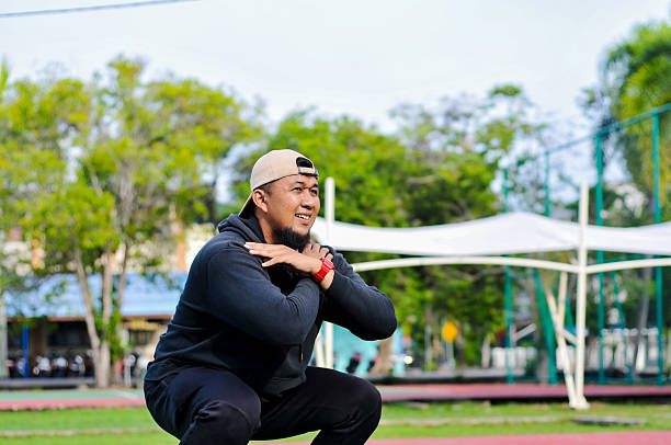 A Concentrated Man Performing a Bodyweight Squat Exercise with Hands Clasped in a Natural Outdoor Sport Environment