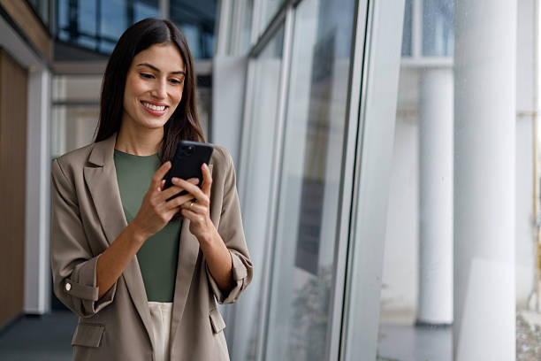istock Businesswoman standing in modern office building and smiling while using app on smartphone, engaging in digital communication 2240921965