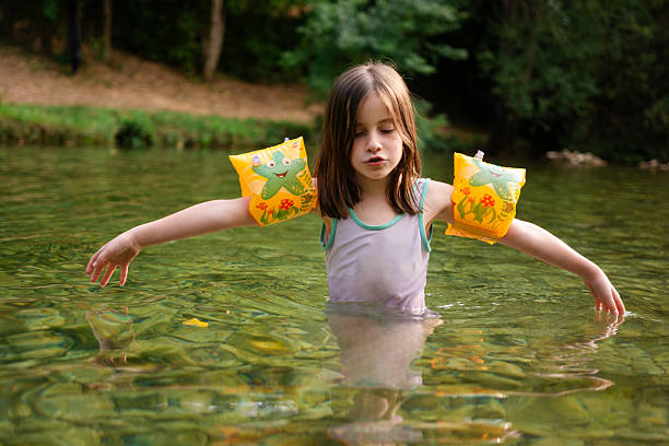 Cute little girl whit brown hair whit raised arms enjoying her summer day in the river