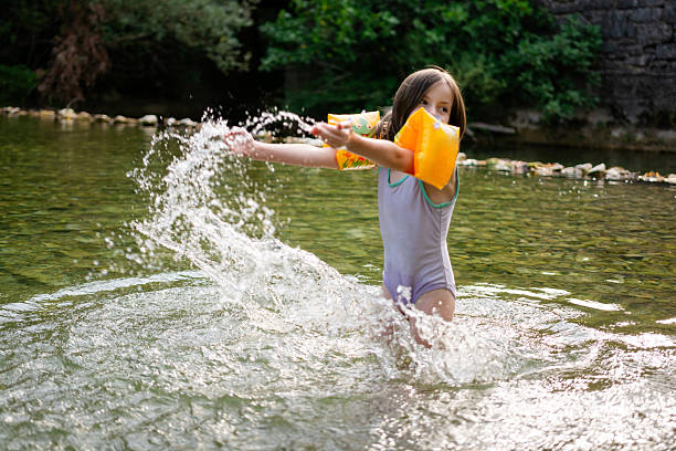 Cute little girl having fun splashing water in the river at summer