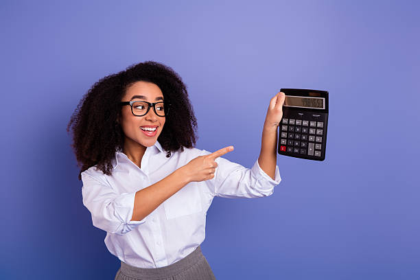 istock Cheerful woman demonstrating a calculator while addressing a business concept, standing against a purple background in formal attire. 2240925573
