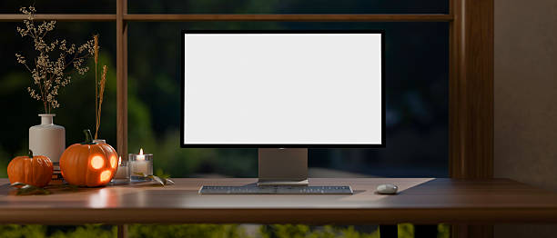 istock White screen computer and jack-o-lantern halloween pumpkins and candles on wooden table aside window 2240926889