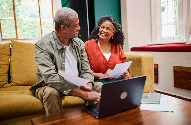 istock Happy Senior Black Couple Smiling while Reviewing Documents on Laptop 2240927340