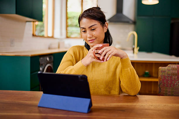 istock Asian Woman Enjoying Coffee While Using Digital Tablet in Kitchen 2240928025