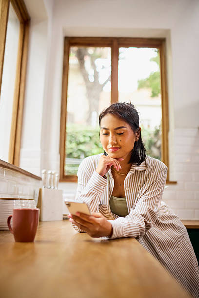 istock Young Asian Woman Focused on Smartphone Leaning on Kitchen Counter 2240928269